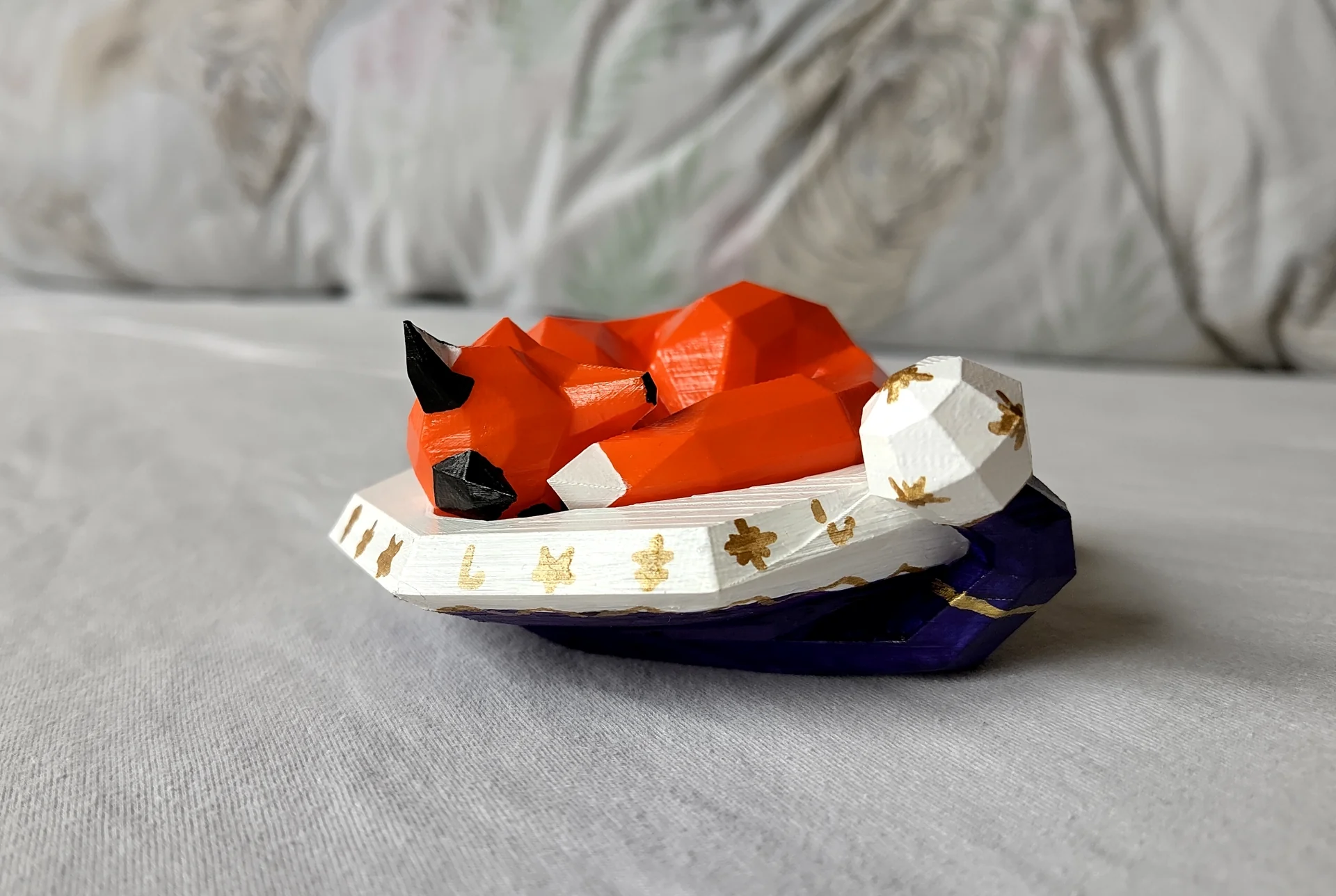 A 3D printed orange fox sleeping in a large purple and white festive hat with golden ornaments.